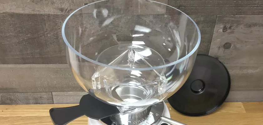 A close-up of an empty, transparent hopper attached to a DISCONTINUED Fiorenzato F4 Nano V2 Espresso Coffee Grinder with a black lid on the wooden countertop. Gray wooden panels are visible in the background. © 2025 1st-line.com