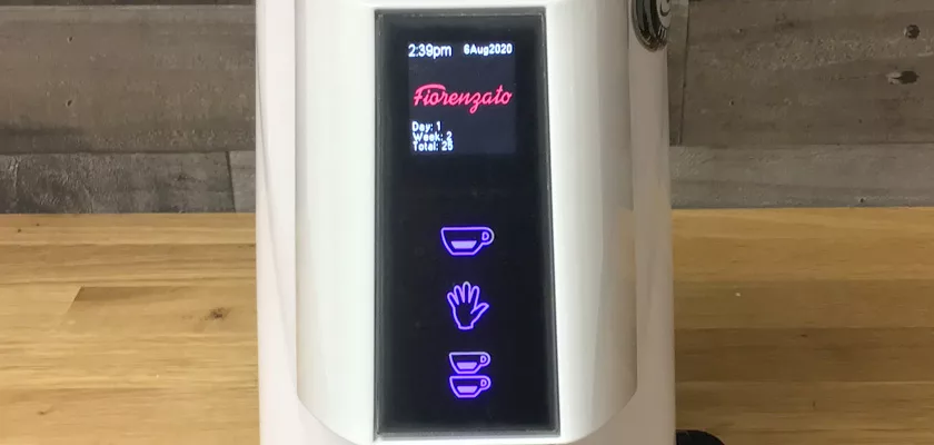 A close-up of the DISCONTINUED Fiorenzato F4 Nano V2 Espresso Coffee Grinder’s digital display shows time, date, usage stats, and illuminated touch icons for coffee and cleaning on a wooden countertop. © 2025 1st-line.com