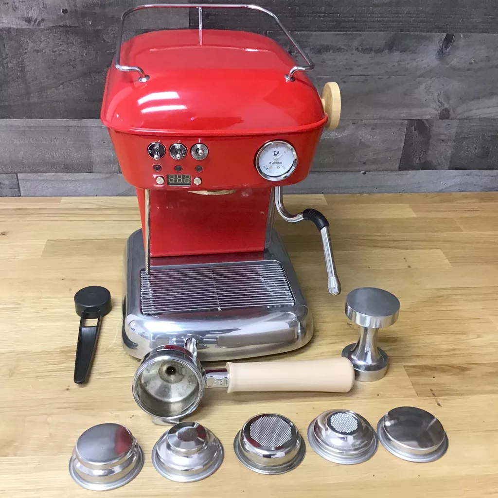 A refurbished SOLD Ascaso Dream UP V3 Love Red PID Espresso Machine with WOOD handle and steam knob rests on a wooden surface, surrounded by espresso accessories like a portafilter, tamper, scoop, and filter baskets. © 2025 1st-line.com