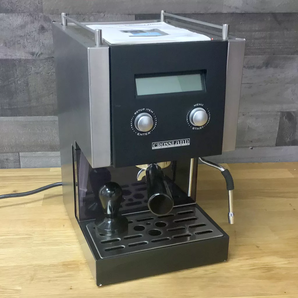 A (SOLD) SIDEWALK SALE - Crossland Coffee CC1 PID Espresso Machine in silver and black sits on a wooden countertop with a digital display, two control knobs, steam wand, portafilter, and tamper against a textured gray wall. © 2025 1st-line.com