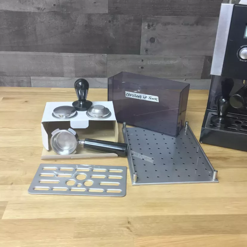 Crossland Coffee CC1 PID Espresso Machine and accessories—portafilter, tamper, metal drip tray, Crossland EV Tank water tank, and stand—displayed on a wooden counter. Product: (SOLD) SIDEWALK SALE - Crossland Coffee CC1 PID Espresso Machine. © 2025 1st-line.com