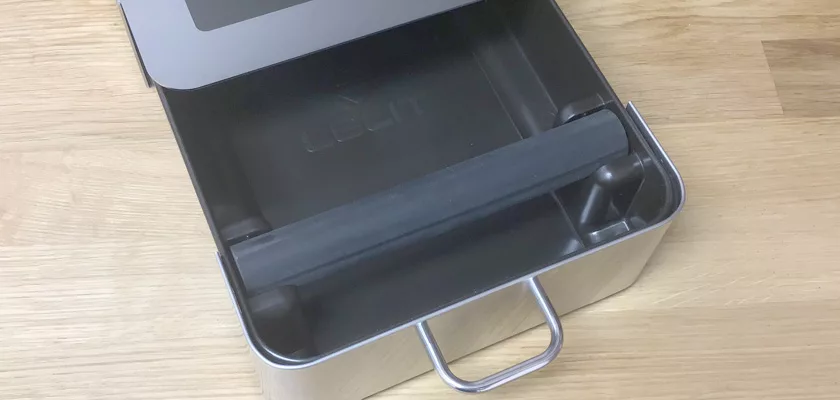 A close-up of the Lelit PLA360M Knock Box Drawer w/ Cloth & Brush, a sleek coffee accessory with a handle and black removable tray, shown on a wooden surface. © 2025 1st-line.com