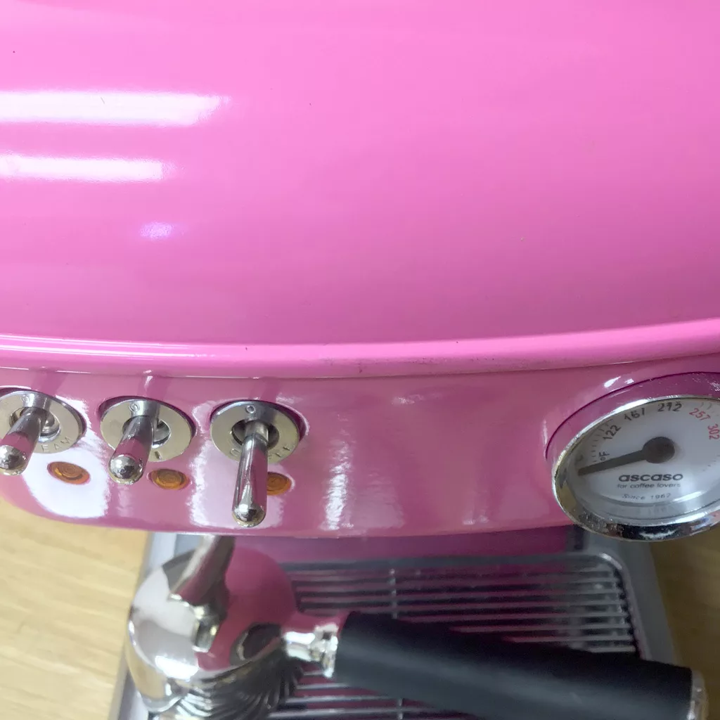 Close-up of a (SOLD) SIDEWALK SALE - Ascaso Dream V2 Strawberry Gum Espresso Machine (Returned & Refurbished) showing three metal switches, a round temperature gauge, and attached portafilter above a metal drip tray. © 2025 1st-line.com