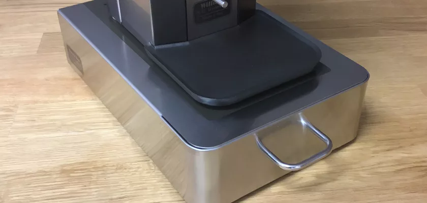 The Lelit PLA360M Knock Box Drawer w/ Cloth & Brush is a rectangular stainless steel espresso accessory with a handle, shown on wood under a coffee machine—perfect for keeping your setup tidy. © 2025 1st-line.com