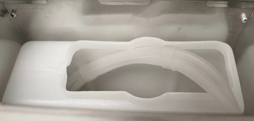 A close-up of a white plastic container with a transparent coiled tube inside the metallic Bezzera New Hobby Espresso Machine—ideal for those exploring espresso making as a new hobby. © 2025 1st-line.com