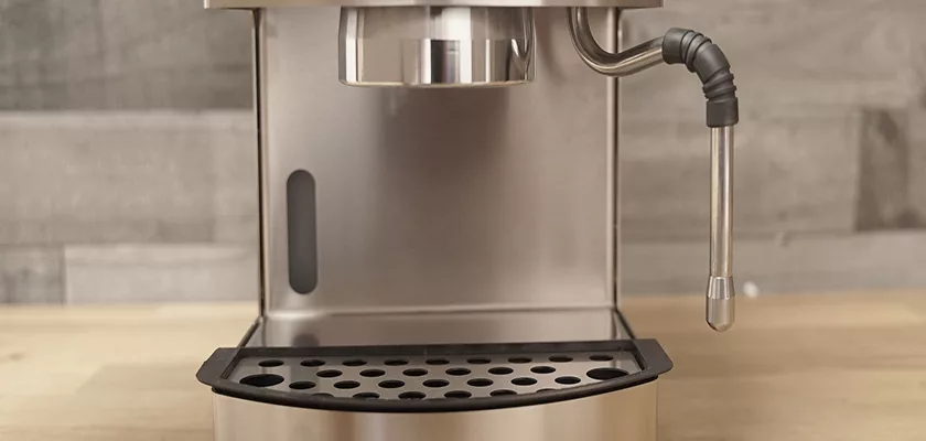 A close-up of the Bezzera New Hobby Espresso Machine highlights its perforated drip tray, right-side steam wand, and partial portafilter holder, all set on a wooden countertop. © 2025 1st-line.com