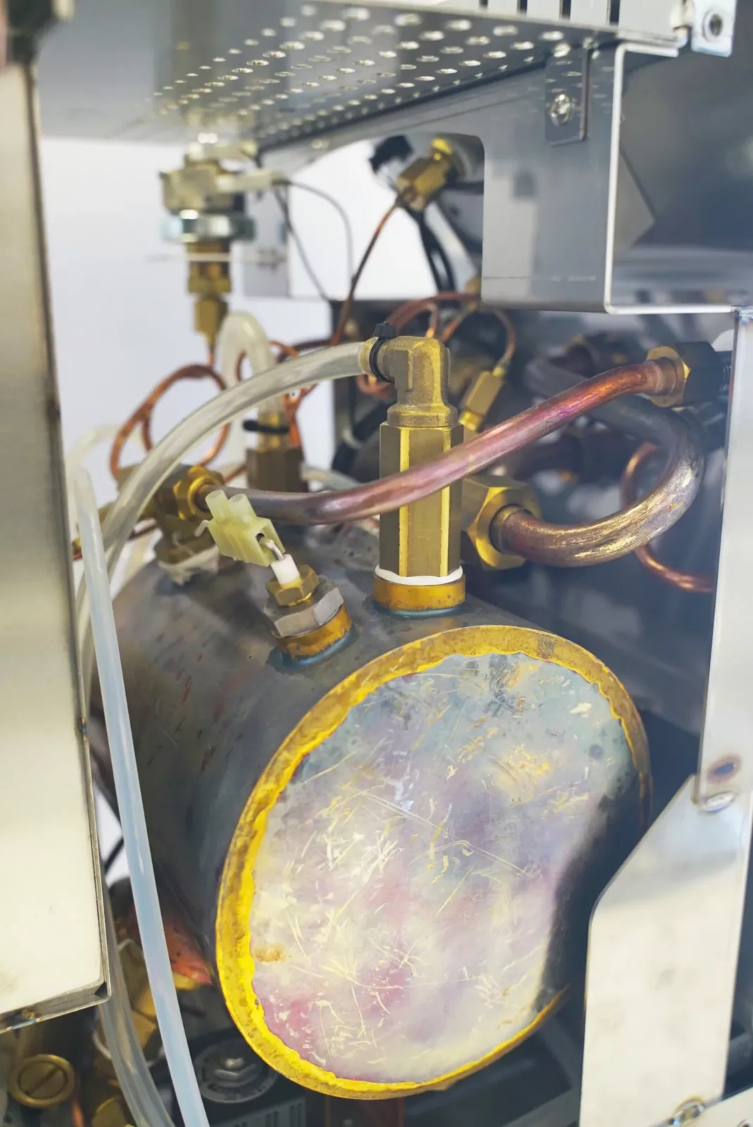 Close-up of internal components in the VBM Domobar Super Analogic HX Espresso Machine w/ Flow Control, showcasing its cylindrical metal boiler, flow control system, copper pipes, brass fittings, and plastic tubes. © 2025 1st-line.com