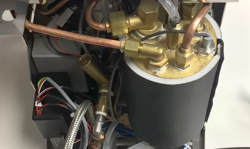 Close-up of the internal components of the VBM Junior Digital HX Espresso Machine w/ Flow Control, highlighting copper pipes, brass fittings, electrical wires, and a cylindrical black insulation piece. © 2025 1st-line.com