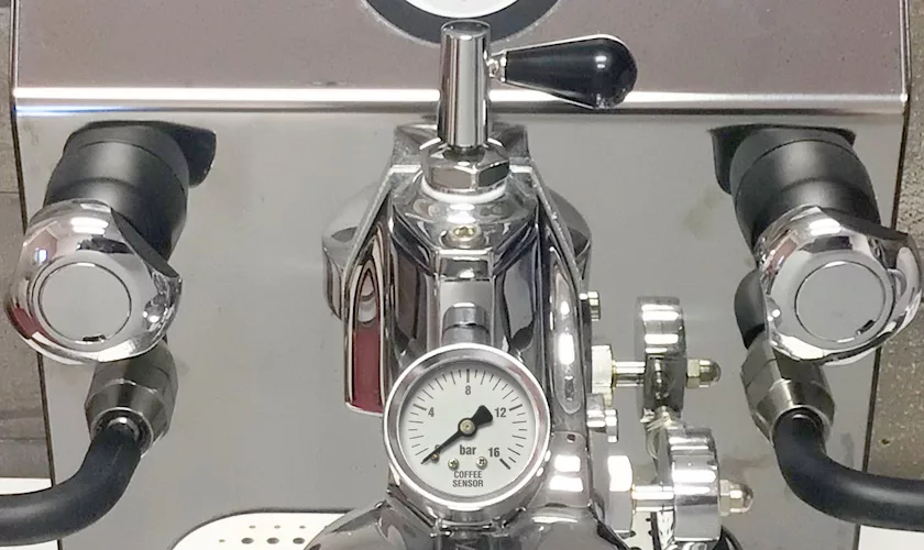 Close-up of the VBM Domobar Super Analogic HX Espresso Machine w/ Flow Control, featuring a central “Coffee Sensor” pressure gauge, two portafilter handles, top flow control lever, and bright reflective stainless-steel surfaces. © 2025 1st-line.com