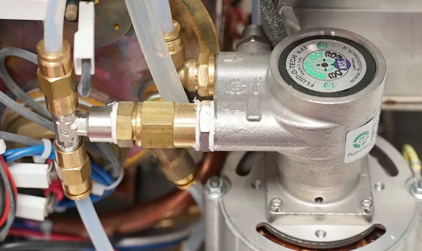 Close-up view of metal and plastic components, pipes, and fittings inside the VBM Domobar Super Analogic HX Espresso Machine with Flow Control. Some parts feature visible labels and markings. © 2025 1st-line.com