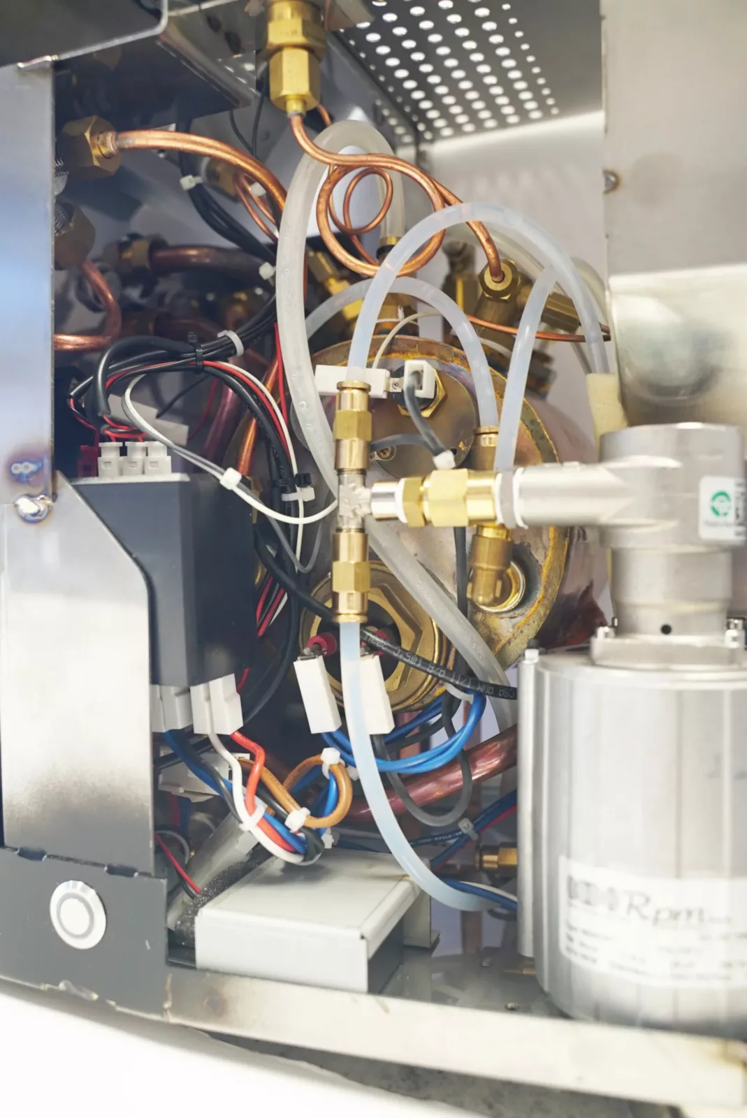 The image displays the internal components of the VBM Domobar Super Analogic HX Espresso Machine w/ Flow Control, revealing tubes, wires, brass fittings, and a motor that highlight its advanced mechanical and electrical systems. © 2025 1st-line.com