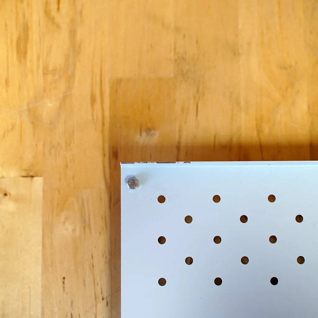 A close-up of the SIDEWALK SALE-VBM White Junior WHITE Drip Tray, Grill & Water Tank Cover E209 featuring a metal grill with small holes and a screw in the top left corner, shown on a light wooden surface. © 2025 1st-line.com