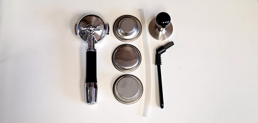 A portafilter, three metal filter baskets, a plastic straw, a metal tamper, a cleaning brush, and the SIDEWALK SALE-VBM White Junior WHITE Drip Tray, Grill & Water Tank Cover E209 are neatly arranged on a white surface. © 2025 1st-line.com