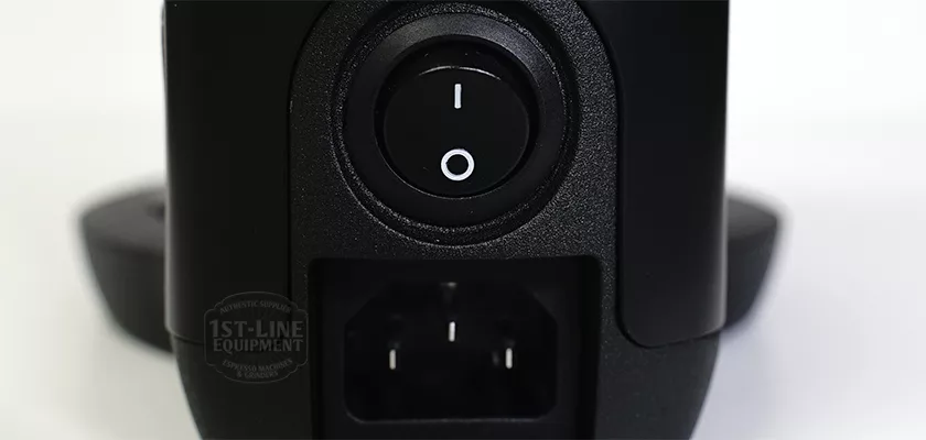 Close-up of a black power switch in the off position above a three-prong socket on the DISCONTINUED PUQPRess Mini Home Precision Coffee Tamper (53.0–58.3mm); part of the 1st-Line Equipment logo appears to the left. © 2025 1st-line.com