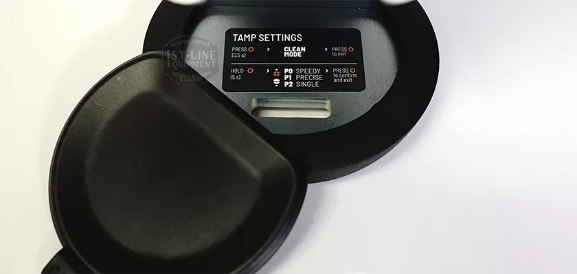 Close-up of the DISCONTINUED PUQPRess Mini Home Precision Coffee Tamper (53.0 to 58.3mm) with its lid open, showing an internal label detailing tamp settings, button instructions, and available mode options. © 2025 1st-line.com