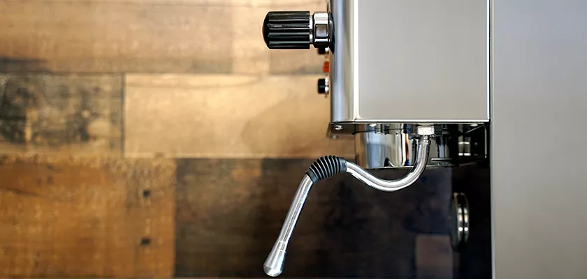 Close-up of the SIDEWALK SALE-VBM White Junior WHITE Drip Tray, Grill & Water Tank Cover E209, featuring a stainless steel steam wand with a curved, ribbed design and control knob, set against a wood-patterned background. © 2025 1st-line.com