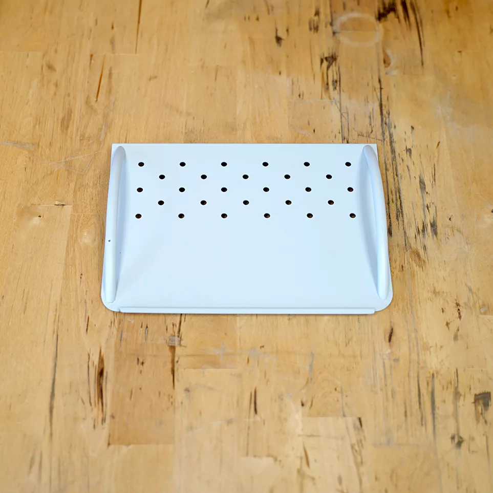 The SIDEWALK SALE-VBM White Junior WHITE Drip Tray, Grill & Water Tank Cover E209 features multiple small round holes and rests on a light wooden surface with visible grain and marks. © 2025 1st-line.com
