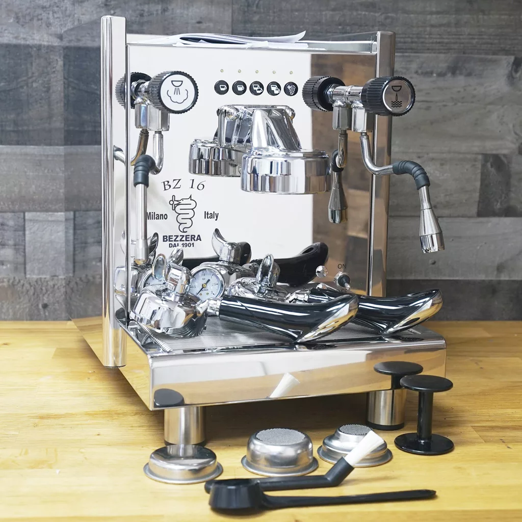 A SOLD - Bezzera BZ16 DE HX Electronic Espresso Machine (returned & refurbished) with two group heads sits on a wooden counter, surrounded by coffee accessories, against a gray wooden wall. © 2025 1st-line.com