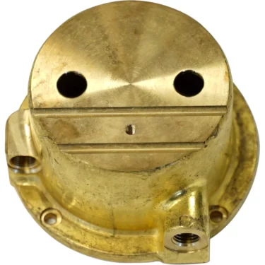 A round brass part for the Elekta 06501014 Coffee Boiler, featuring three holes and a raised section that gives it a face-like appearance with two large eyes and a straight mouth when seen from above. © 2025 1st-line.com