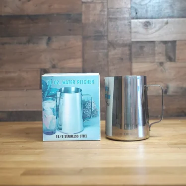 A SIDEWALK SALE - Water Pitcher 70 OZ. sits on a wooden surface beside its box, which displays an image and product specs. A wood-paneled wall is visible in the background—an ideal find for your next Sidewalk Sale!. © 2025 1st-line.com