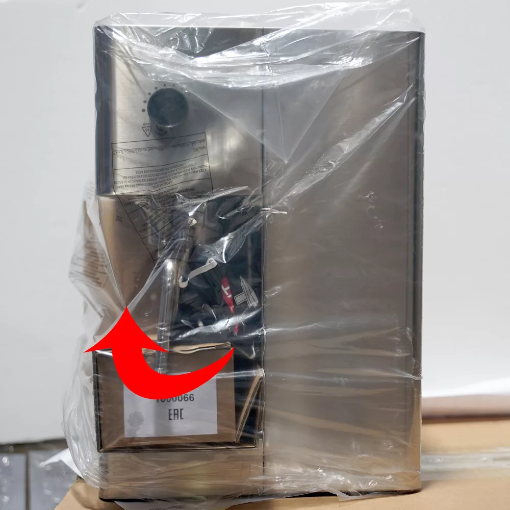 A stainless steel Lelit Elizabeth appliance wrapped in clear packaging, with a red arrow pointing to a label on the front. The label displays text and a barcode. The appliance is set against a white wall background. © 2025 1st-line.com