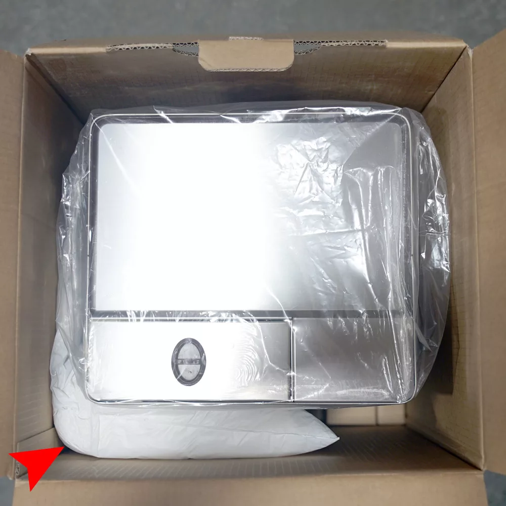 The Lelit Elizabeth, securely wrapped in protective packaging, rests inside a cardboard box with foam padding. This rectangular metal appliance features a small circular dial and a convenient tray. © 2025 1st-line.com