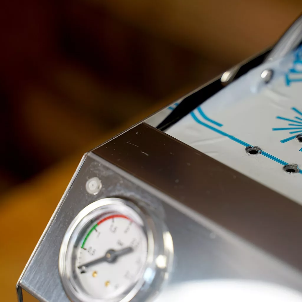 A close-up of the SIDEWALK SALE - VBM Domobar Super HX Tank Espresso Machine DEMO (E114) shows its round pressure gauge with red/green scale, glossy finish, and part of a digital panel with blue graphics and text. © 2025 1st-line.com