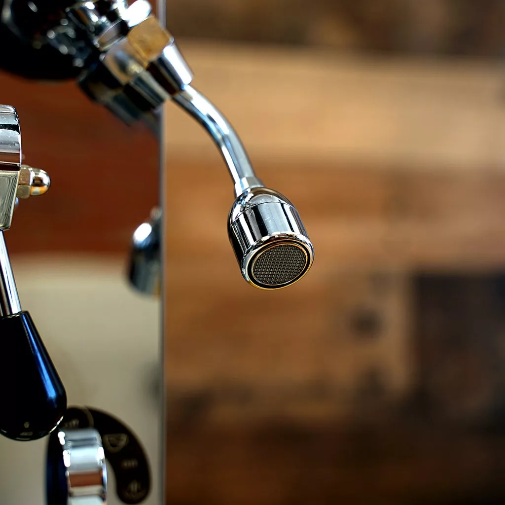 Close-up of a shiny metal steam wand on the SIDEWALK SALE - VBM Domobar Super HX Tank Espresso Machine DEMO (E114), with a blurred wooden background. The focus is on the tip, used for steaming milk for coffee drinks. © 2025 1st-line.com