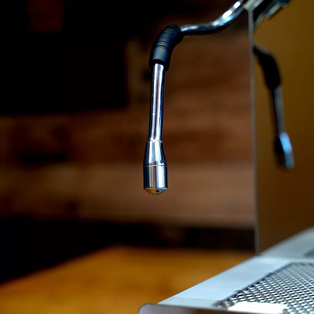 Close-up of the metal steam wand on the SIDEWALK SALE - VBM Domobar Super HX Tank Espresso Machine DEMO (E114), focusing on the tip used for steaming milk, with a blurred brown and yellow background. © 2025 1st-line.com