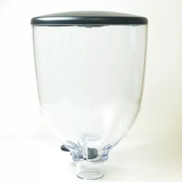 The Compak K..286 COMPLETE BEAN HOPPER is a clear, empty bean dispenser with a black lid and bottom spigot, shown against a plain white background. © 2025 1st-line.com