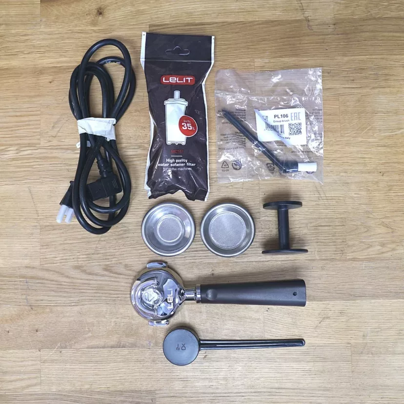 Accessories for the (SOLD) SIDEWALK SALE - 2020 Lelit Victoria PL91T PID Single Boiler Espresso Machine E113 include a power cord, water filter, two metal filter baskets, portafilter, measuring spoon, black plastic tamper, and cleaning tool. © 2025 1st-line.com