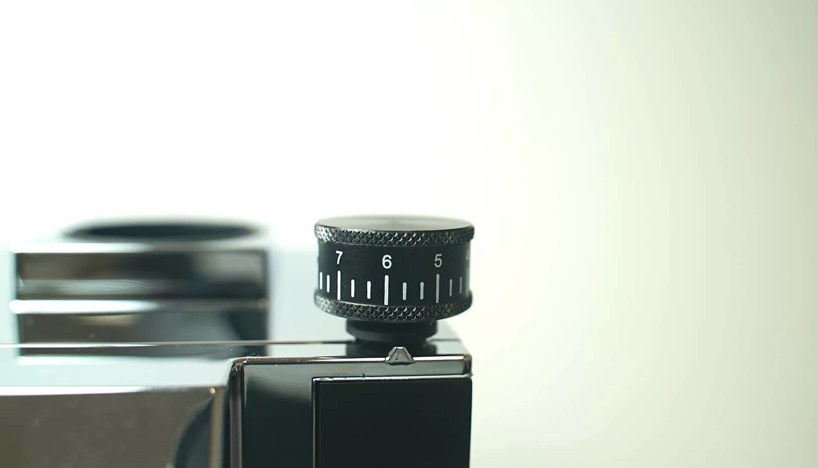 Close-up of a black numeric dial set to 7 on the shiny Eureka Oro Mignon XL Espresso Coffee Grinder, attached to a metallic device against a plain light background. © 2025 1st-line.com