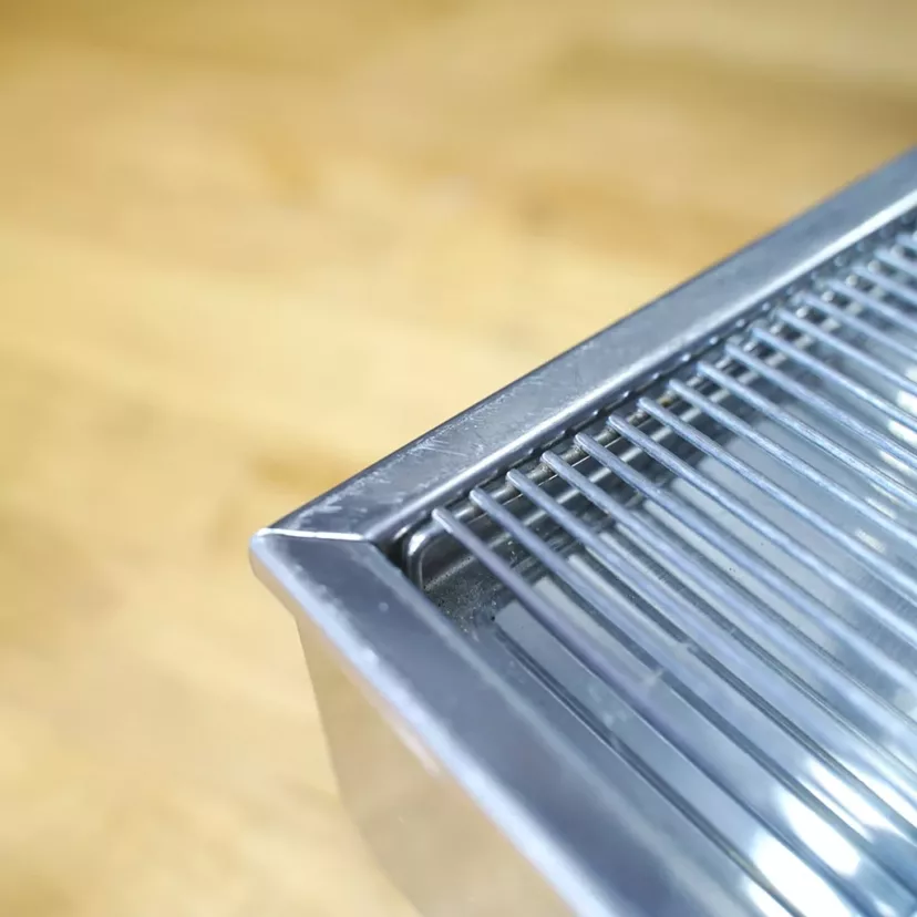 Close-up of the stainless steel wire rack corner from the (SOLD) SIDEWALK SALE - USED 2003 Elektra A3 Sixties Deliziosa Semi Automatic HX Espresso Machine E014, placed on light wood, focusing on its metal bars and frame with a blurred background. © 2025 1st-line.com
