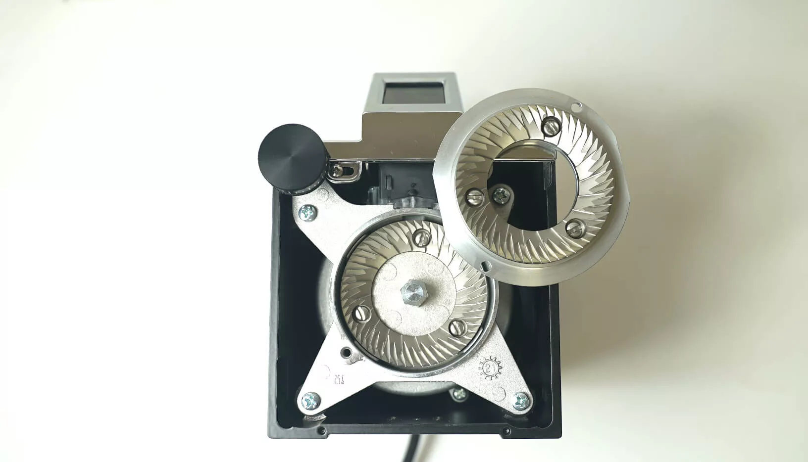 Top-down view of the Eureka Oro Mignon XL Espresso Coffee Grinder with its burrs exposed, revealing the metal grinding mechanism and screws inside a rectangular black casing on a white surface. © 2025 1st-line.com