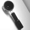 A CAPSULE FILTER HOLDER PORTAFILTER FOR CIMBALI with a black handle rests angled on a white surface. In black and white, the photo highlights its metallic and matte textures, showcasing this classic espresso accessory. © 2025 1st-line.com