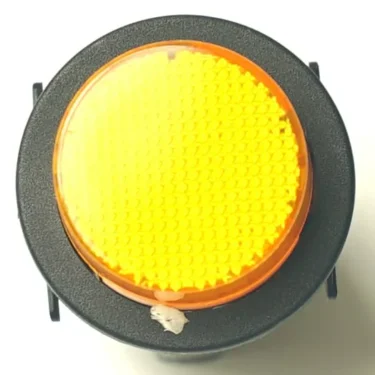 A close-up of the V.4331 YELLOW MOMENTARY PUSH SWITCH, a round pedestrian crossing button with a textured yellow surface on a black base. A small piece of white debris is visible near the bottom. © 2025 1st-line.com