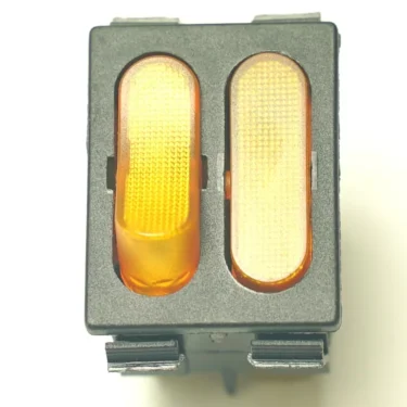 A close-up of the V.4383 YELLOW ROCKER SWITCH + PILOT, a rectangular electronic switch featuring two orange illuminated buttons—one pressed—set within a gray plastic casing. © 2025 1st-line.com