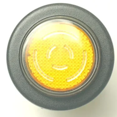 Close-up of a round, textured yellow push button with a black outer ring and concentric arc patterns, resembling the V.4250 25mm LIGHT STEAM SWITCH, which is commonly used on pedestrian crossing signal poles. © 2025 1st-line.com