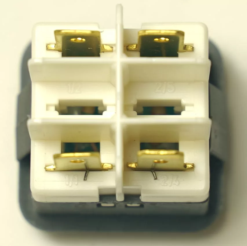 Close-up of a V.4216 15.2mm DIAMETER RED PUSH-BUTTON featuring a white, square electrical connector with four brass terminals in a 2x2 grid, mounted on a black base. Terminals are spaced 15.2mm apart for secure connections. © 2025 1st-line.com