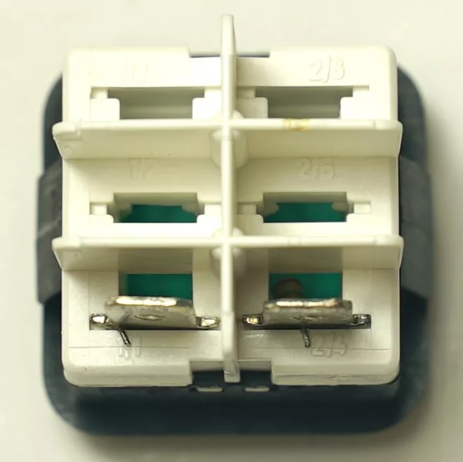 Close-up of the V.4418 INDICATOR LIGHT, a white plastic connector with four metal prongs, grid dividers, and engraved numbers—suitable for indicator light applications against a neutral background. © 2025 1st-line.com