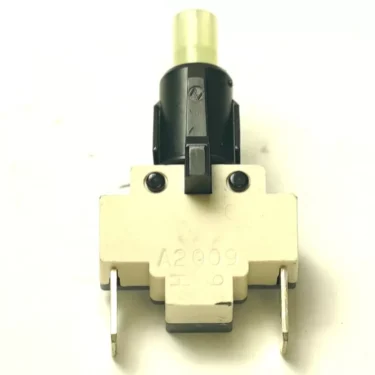 Close-up of the W.5072 250V 16A PUSH-BUTTON switch with a white rectangular base, two metal prongs at the bottom, and a black and yellow push-button on top, photographed against a white background. © 2025 1st-line.com