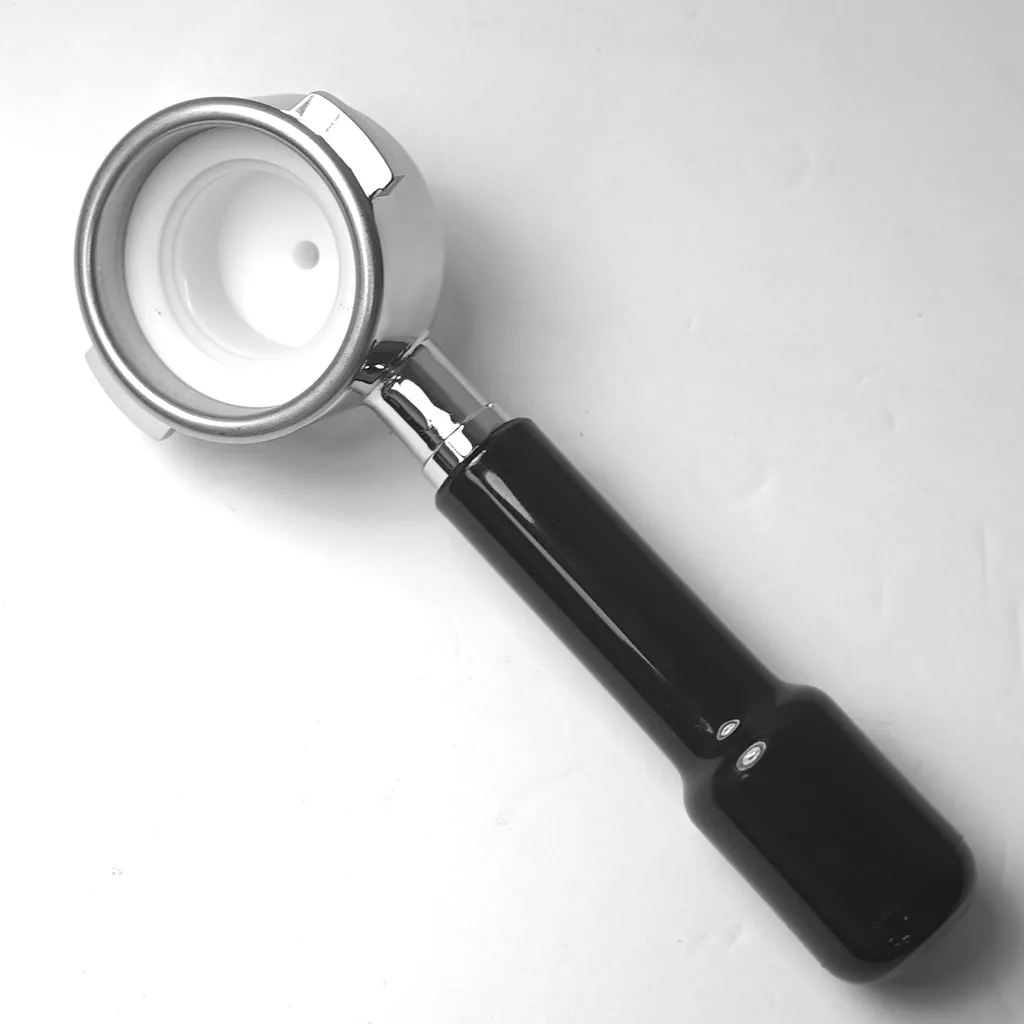 The CAPSULE FILTER HOLDER FOR SPAZIALE, a metal espresso portafilter with a black handle, is resting on a white surface and viewed from above. © 2025 1st-line.com