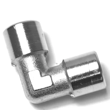 The V.1867 1/8F Elbow Fitting features a shiny metallic finish, a 90-degree angle, and cylindrical openings on both ends, shown against a white background. © 2025 1st-line.com