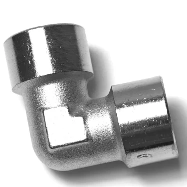 The V.1868 1/2F Elbow Fitting is a shiny metal piece with threaded openings on both ends, shown on a white background. © 2025 1st-line.com