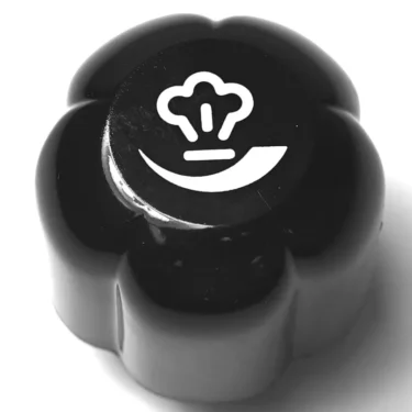 The W26003 TOP QUALITY LEVER ROD is a black, flower-shaped oven knob with a white chef hat and smiley face icon on top, offering smooth and reliable control. © 2025 1st-line.com