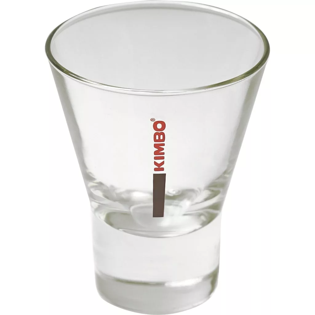 A clear, empty glass espresso shot glass with a thick base. KIMBO is printed vertically in red beside a brown stripe—ideal for dosing shots from your DISCONTINUED Mazzer SMISCAEU6/QQQ Short Bean Hopper Assembly (320g). © 2025 1st-line.com