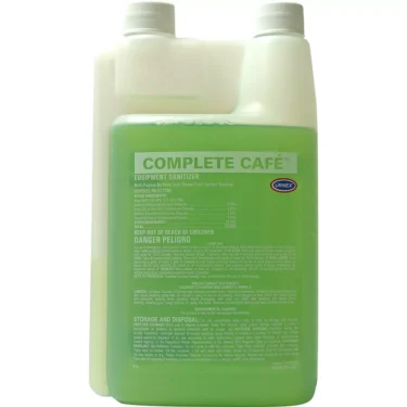 A clear plastic container of Urnex Complete Cafe Equipment Sanitizer (green liquid) with measurement markings and a large label displaying product details, usage instructions, and safety warnings. © 2025 1st-line.com