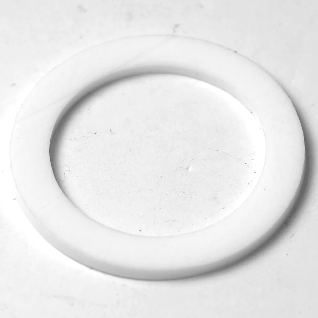 A close-up of a white, flat washer—used to seal connections in the F.1402 FAEMA E-91/DUE Stainless Steel Steam Wand—lying on a smooth, light-colored surface. © 2025 1st-line.com