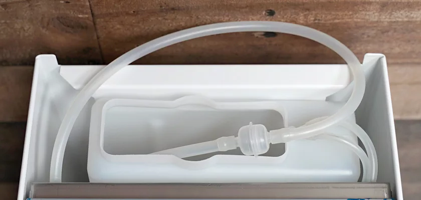 A close-up of a white plastic water tank with an attached flexible tube inside a rectangular compartment, part of the Bezzera Crema PM HX Espresso Machine. © 2025 1st-line.com