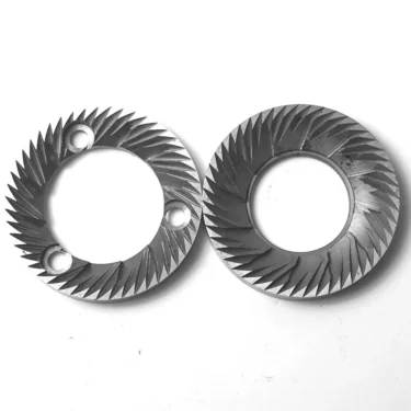 A pair of MG..21 CUNILL BLADES GRINDING BURRS 59mm, featuring sharp, angled ridges and holes, are displayed side by side on a white background. © 2025 1st-line.com